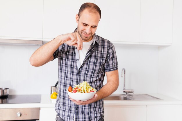 Portret van een glimlachende mens die het zout op salade in de keuken kruiden