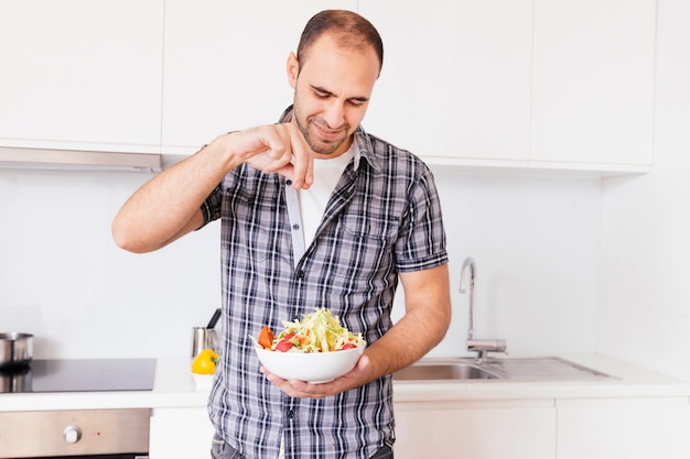 Portret van een glimlachende mens die het zout op salade in de keuken kruiden