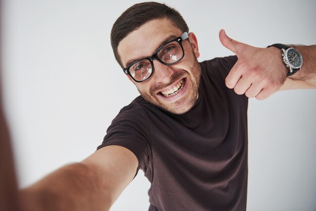 Portret van een glimlachende mens in glazen die duim over wit tonen