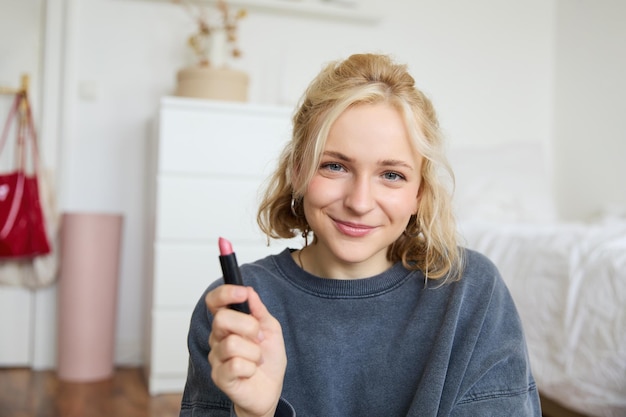 Portret van een glimlachende mooie vrouw in haar kamer die zit en lippenstift toont en haar favoriet aanbeveelt