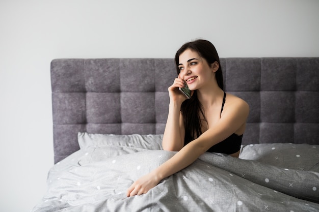 Portret van een glimlachende mooie vrouw in lingerie liggend op het bed en praten over de telefoon