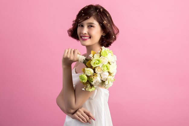 Portret van een glimlachende speelse leuke die bloemen van de vrouwenholding op roze worden geïsoleerd