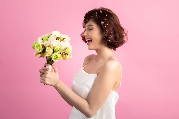 Portret van een glimlachende speelse leuke die bloemen van de vrouwenholding op roze worden geïsoleerd