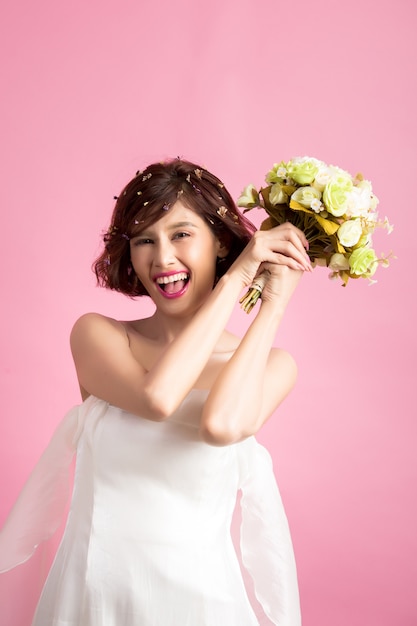 Portret van een glimlachende speelse leuke die bloemen van de vrouwenholding op roze worden geïsoleerd