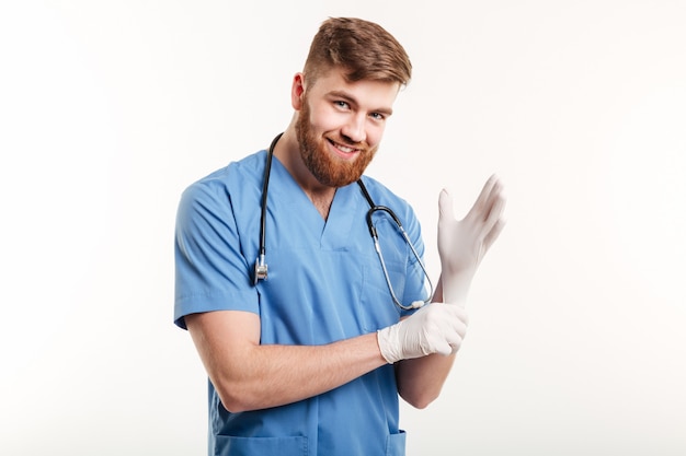 Portret van een glimlachende vriendschappelijke arts die op steriele handschoenen zet