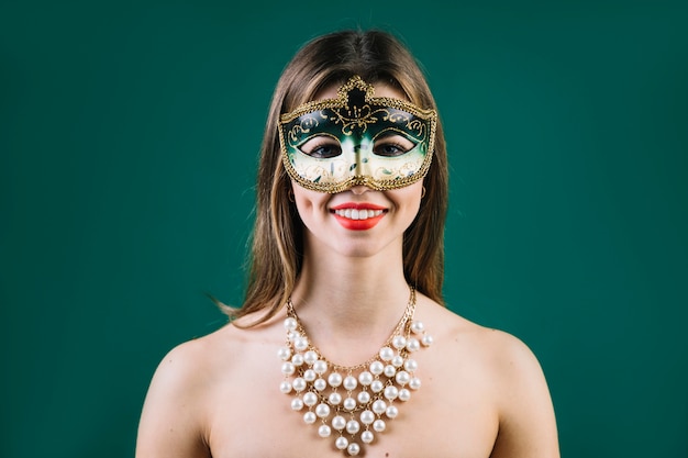 Portret van een glimlachende vrouw die Carnaval-masker op gekleurde achtergrond draagt