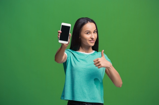 Portret van een glimlachende vrouw die het lege smartphonescherm toont dat op groen wordt geïsoleerd