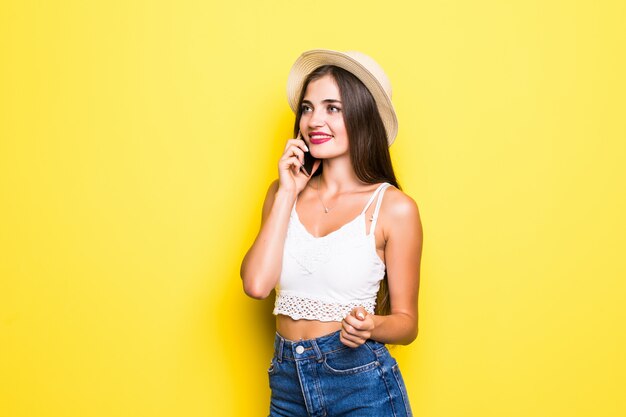 Portret van een glimlachende vrouw die op de telefoon over gele muur spreekt