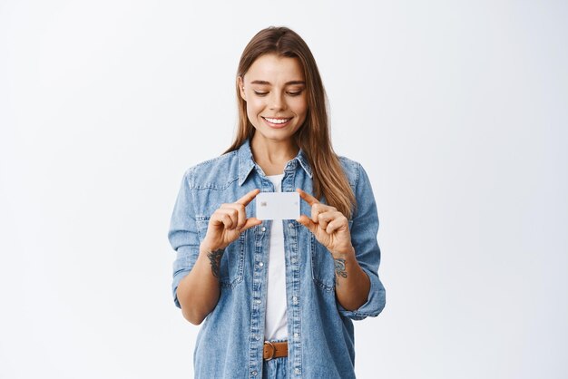 Portret van een glimlachende vrouw met blond haar die een plastic creditcard toont en er een blije open bankrekening uitziet die tegen een witte achtergrond staat