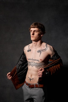 Portret van een hipster persoon met getatoeëerd lichaam in jas poses op donkere achtergrond