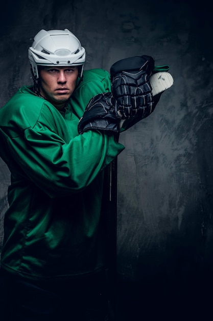 Portret van een hockeyspeler in beschermende kleding houdt een speelstok op een grijze achtergrond.