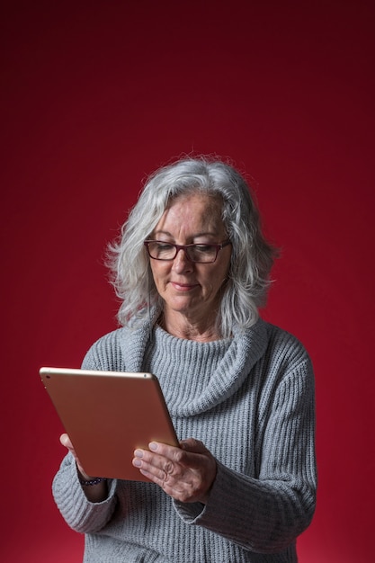 Portret van een hogere vrouw die digitale tablet gebruiken tegen rode achtergrond