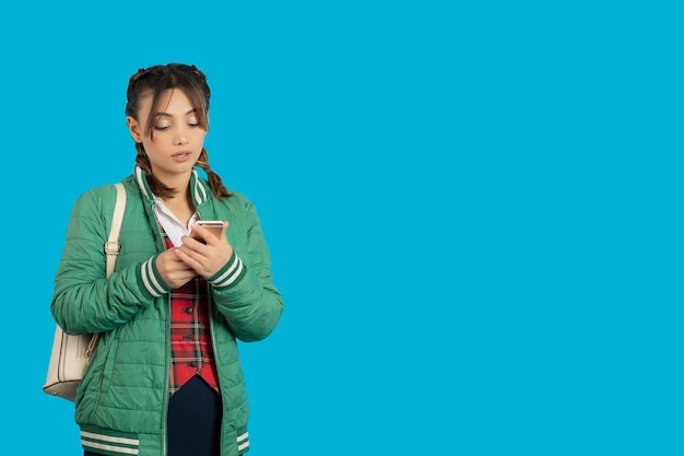 Portret van een jong college meisje dat telefoon vasthoudt en op een blauwe achtergrond staat. Hoge kwaliteit foto