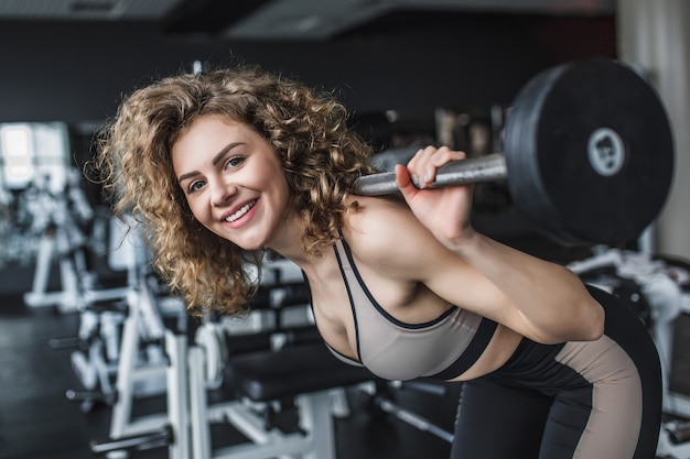 Portret van een jong fitnessmeisje dat squats met barbell doet in de sportschool