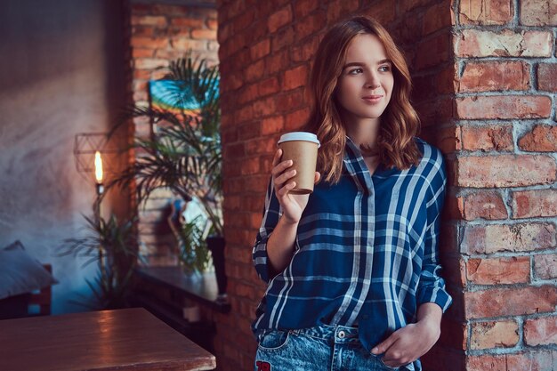 Portret van een jong hipstermeisje drinkt koffie in de ochtend, leunend op