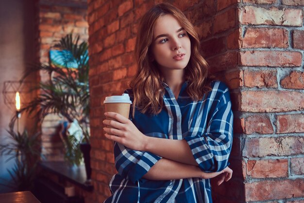 Portret van een jong hipstermeisje drinkt koffie in de ochtend, leunend op