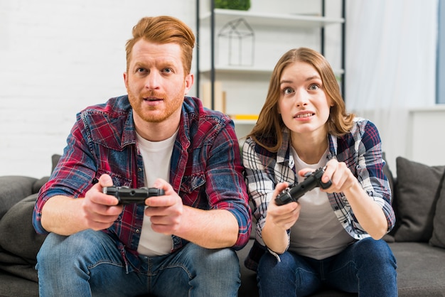 Gratis foto portret van een jong koppel zittend op een zwarte bank het spelen van de video game met joystick