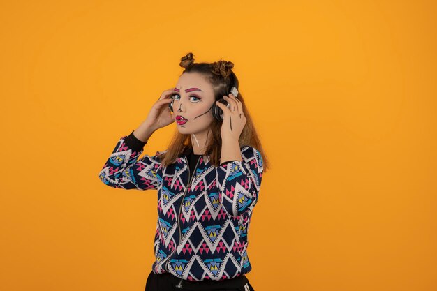 Portret van een jong meisje dat creatieve make-up draagt en muziek luistert op een oranje achtergrond. Hoge kwaliteit foto