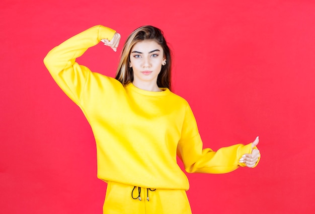 Portret van een jong meisje in een gele outfit die staat en duimen omhoog geeft