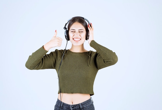 Portret van een jong meisje in een koptelefoon die naar muziek luistert en duimen opgeeft.