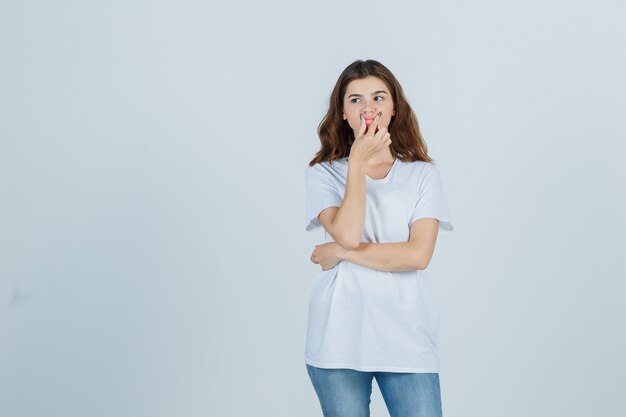 Portret van een jong meisje lippen knijpen in wit t-shirt, spijkerbroek en op zoek doordachte vooraanzicht