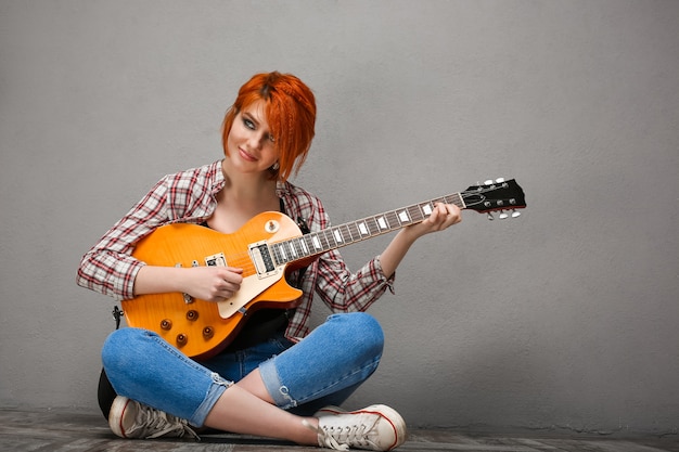 Portret van een jong meisje met gitaar over grijze achtergrond.