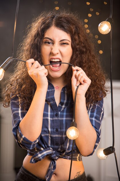 Portret van een jong model in geruit overhemd dat een draad van lampen bijt