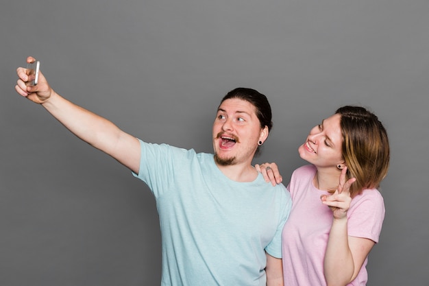 Portret van een jong paar die selfie op slimme telefoon tegen grijze muur nemen