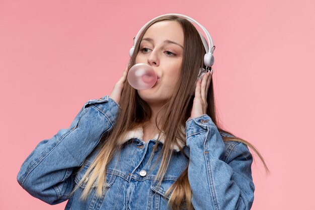 Portret van een jong tienermeisje met een koptelefoon die kauwgomballon blaast