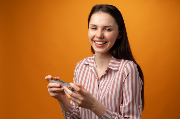 Portret van een jonge aantrekkelijke vrouw die haar smartphone gebruikt tegen een gele achtergrond