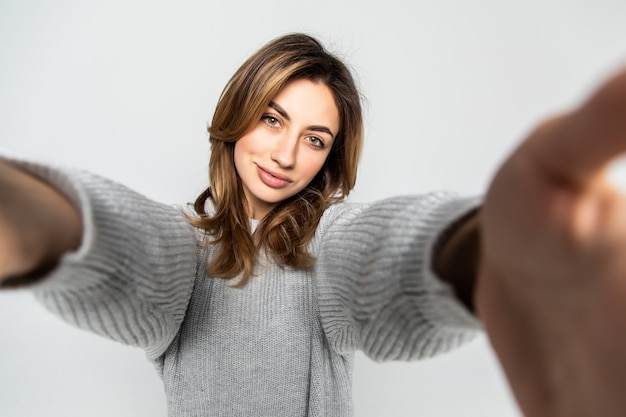 Portret van een jonge aantrekkelijke vrouw die selfie foto op smartphone maken die op een grijze muur wordt geïsoleerd