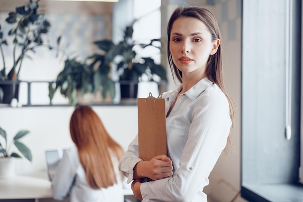 Portret van een jonge aantrekkelijke zakenvrouw die klembord op kantoor houdt