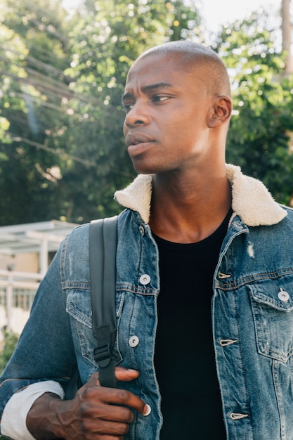 Portret van een jonge Afrikaanse man met een rugzak op zijn schouder wegkijken