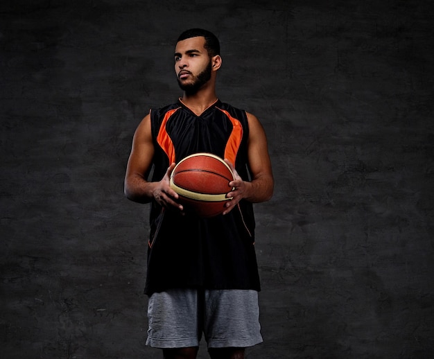 Portret van een jonge Afro-Amerikaanse basketballer in sportkleding geïsoleerd over donkere achtergrond.