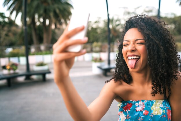 Portret van een jonge afro Amerikaanse Latijns-vrouw die een selfie met mobiele telefoon buiten in de straat.