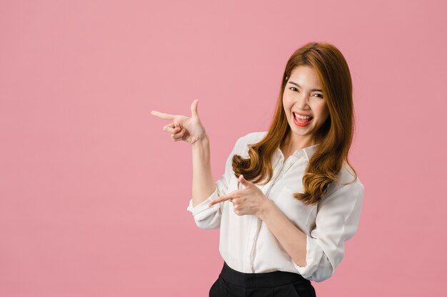 Portret van een jonge Aziatische dame die lacht met een vrolijke uitdrukking, laat iets geweldigs zien op lege ruimte in casual kleding en kijkt naar camera geïsoleerd over roze achtergrond.