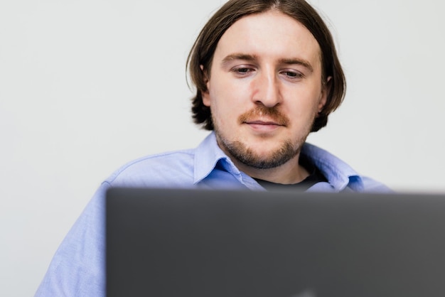 Portret van een jonge, bebaarde man die lacht en een laptop gebruikt terwijl hij thuis op de bank zit