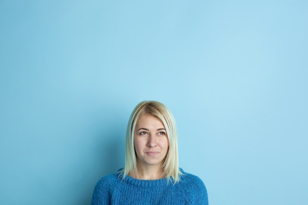 Gratis foto portret van een jonge blanke vrouw ziet er dromerig, schattig en gelukkig uit. denken, afvragen, dromen op blauwe ruimte