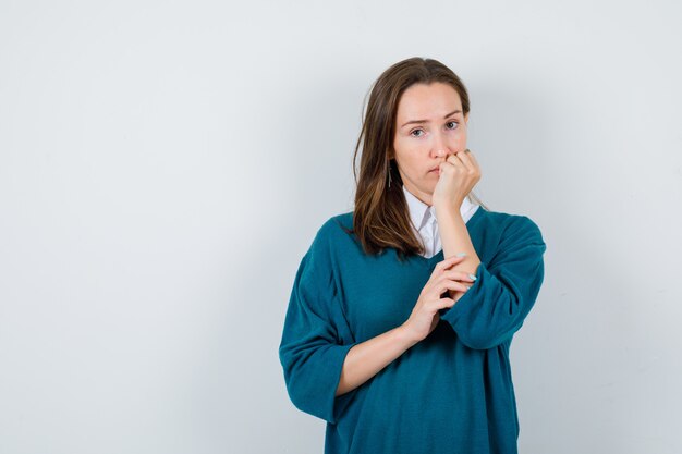 Portret van een jonge dame die de hand op de kin houdt in een wit overhemd, een trui en een peinzend vooraanzicht kijkt