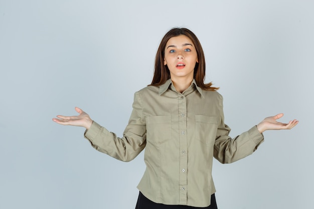 Portret van een jonge dame die een hulpeloos gebaar in shirt, rok toont en een verbaasd vooraanzicht toont