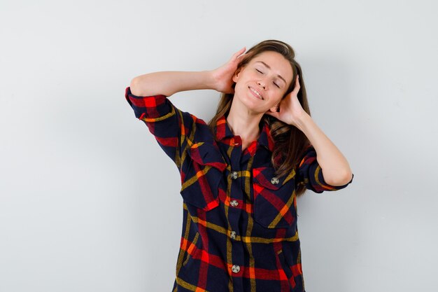 Portret van een jonge dame die haar hoofd in casual overhemd wrijft en ontspannen vooraanzicht kijkt