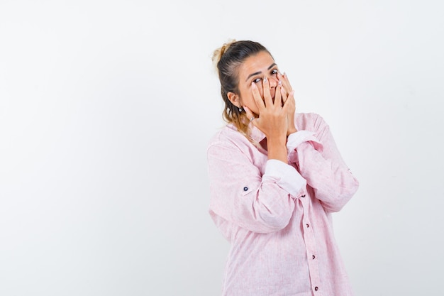 Portret van een jonge dame die handen op de mond in roze overhemd houdt en opgewonden vooraanzicht kijkt