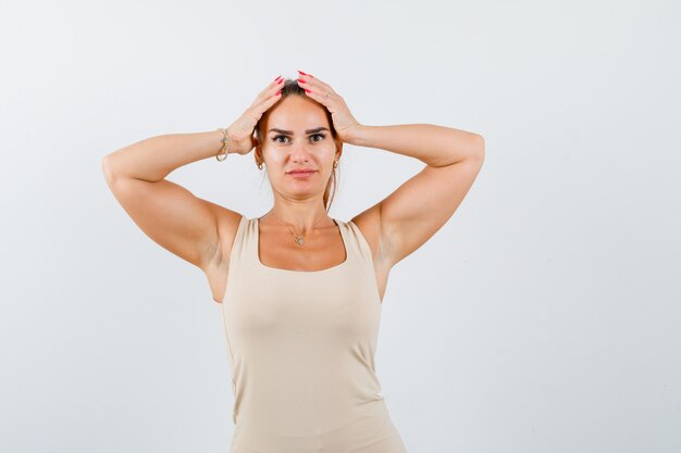 Portret van een jonge dame die handen op het hoofd in tanktop houdt en verbijsterd vooraanzicht kijkt