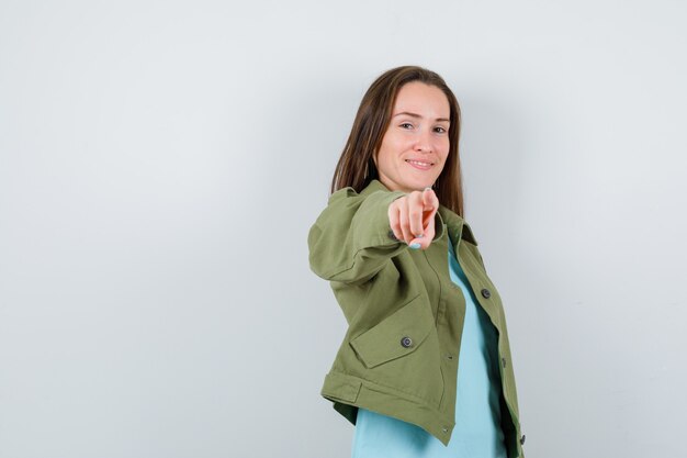 Portret van een jonge dame die naar de camera wijst in t-shirt, jas en er vrolijk vooraanzicht uitziet