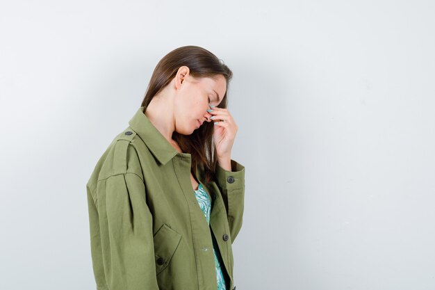 Portret van een jonge dame die neus en ogen in een groene jas wrijft en er vermoeid vooraanzicht uitziet