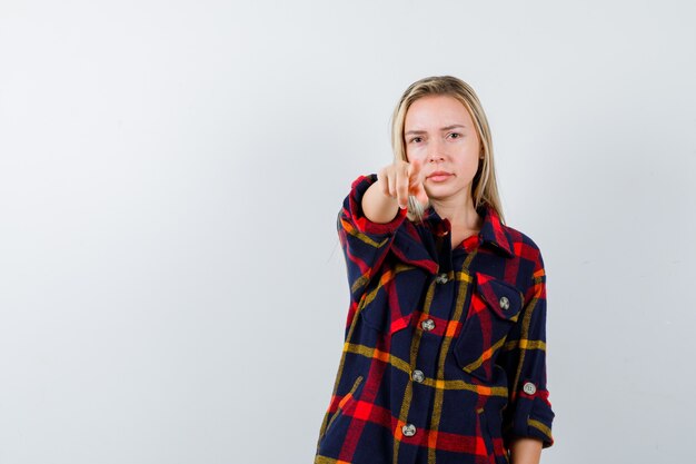 Portret van een jonge dame die op camera in ingecheckte overhemd richt en zelfverzekerd vooraanzicht kijkt