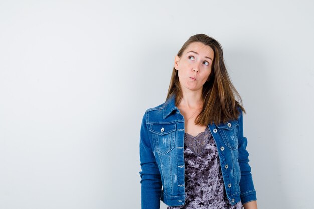 Portret van een jonge dame die opkijkt in blouse, spijkerjasje en peinzend vooraanzicht kijkt