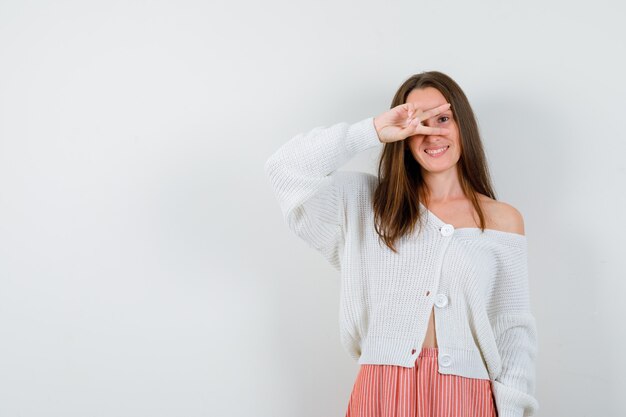 Portret van een jonge dame die overwinningsteken in vest en rok toont die geïsoleerd gelukkig kijken