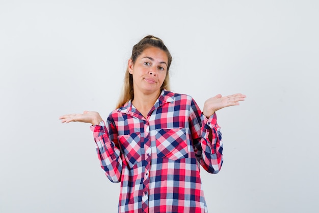 Portret van een jonge dame die verwelkomend gebaar in geruit overhemd toont en zelfverzekerd vooraanzicht kijkt