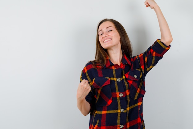 Portret van een jonge dame die winnaargebaar in casual overhemd toont en zalig vooraanzicht kijkt